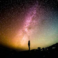 Ancient Japanese Astronomy Silhouetted person stands on a hill, looking up at a vibrant, star-filled night sky. The Milky Way is prominently visible, creating a colorful, luminous pathway across the sky. The horizon glows with a gradient of warm and cool tones.