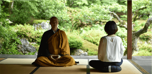 A Japanese monk and tourist sitting peacefully in a temple in a meditative posture practicing Zen meditation.