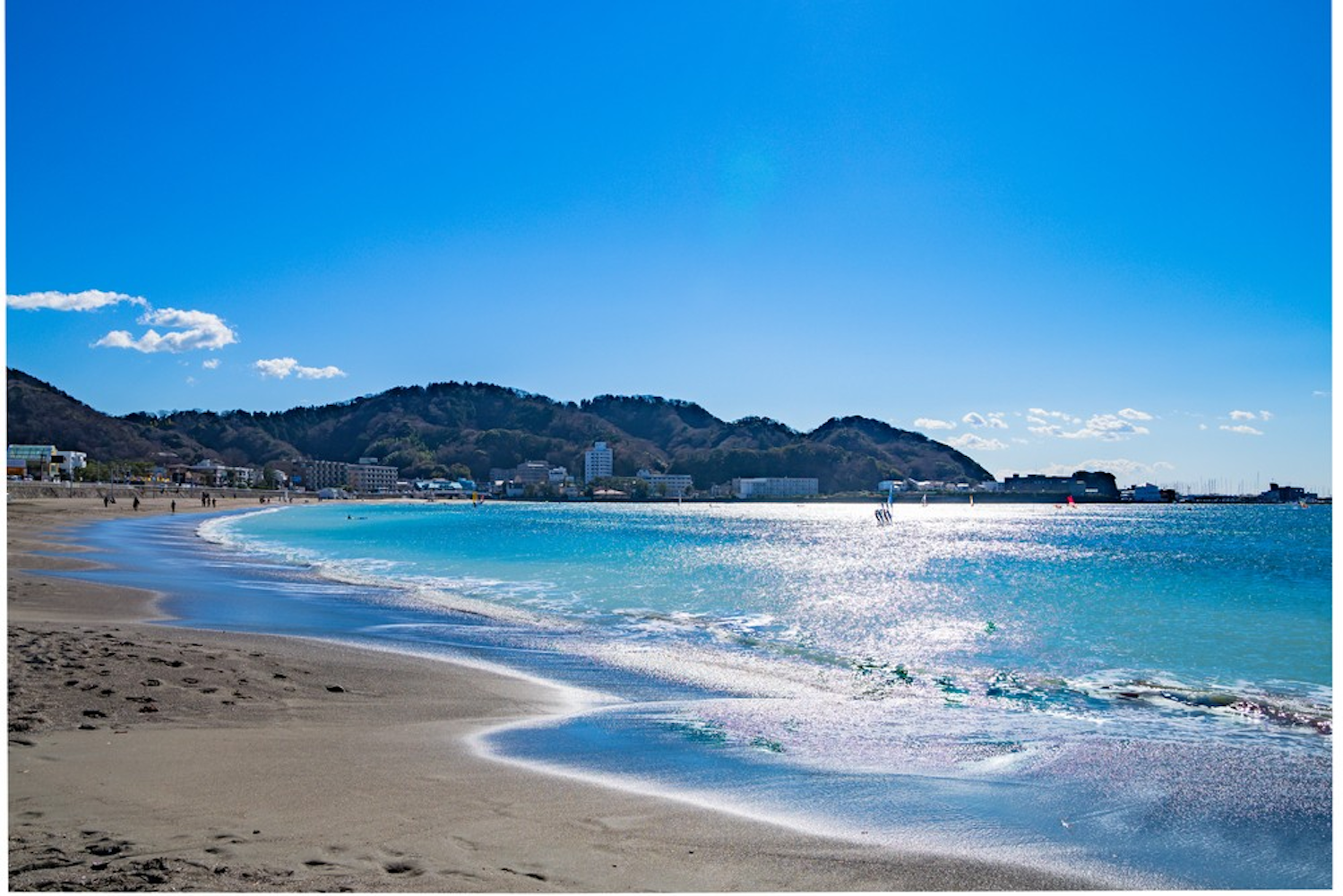 Surreal view of Yuigahama Beach on sunny day in Kamakura, Japan with blue water and a hill in the background.