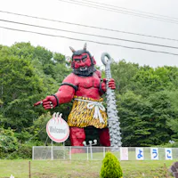 One of the demon statues that mark the way into Noboribetsu Onsen A large red demon statue with a spiked club beside a welcome sign at the entrance to Noboribetsu