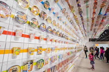 Little girl look up many cup noodles decoration on wall exhibition