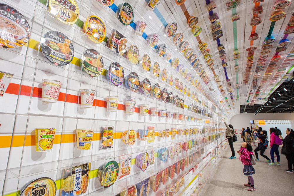 Little girl look up many cup noodles decoration on wall exhibition