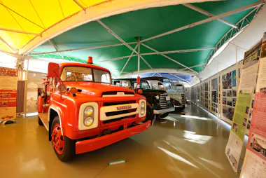 Vintage red fire truck and an old-fashioned bus are displayed indoors under a colorful yellow and green tent, with informational boards and posters lining the walls.