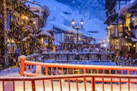 Snow falling at night on the wooden ryokan and gas lamps lining the river in Ginzan Onsen, Yamagata