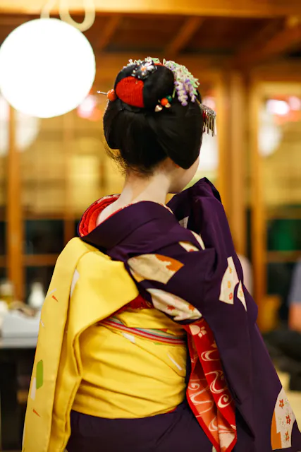 舞伎学徒表演 一位身穿紫色和服、系着黄色带的舞伎学徒从背后所见,身下方有一盏纸灯笼