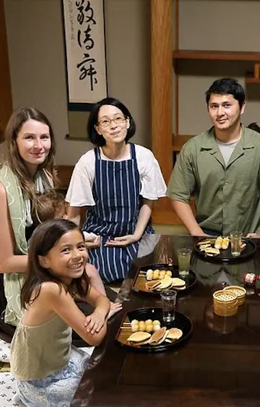 Wagashi Cooking Class Six people sit around a low table with snacks and drinks in a traditional Japanese-style room, smiling and posing for the photo. The room features tatami mats, sliding doors, and decorative calligraphy.