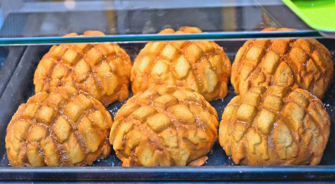 Melon Pan Six conchas, Mexican sweet breads with a grid pattern on top, displayed in a glass case.