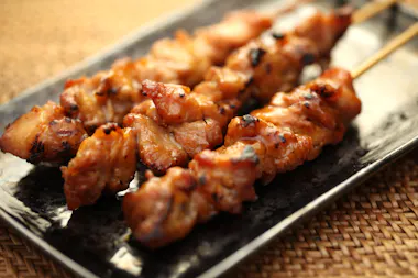 Three skewers of grilled chicken yakitori, glazed and slightly charred, served on a dark rectangular plate on a woven placemat.