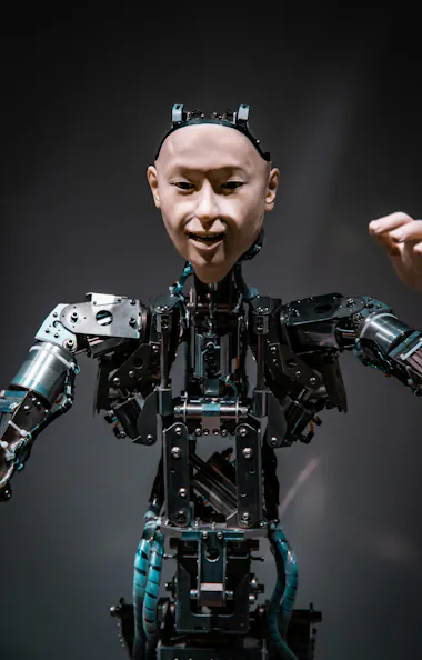 Miraikan Museum A humanoid robot with a realistic human-like face and exposed mechanical parts raises one arm, set against a dark background.