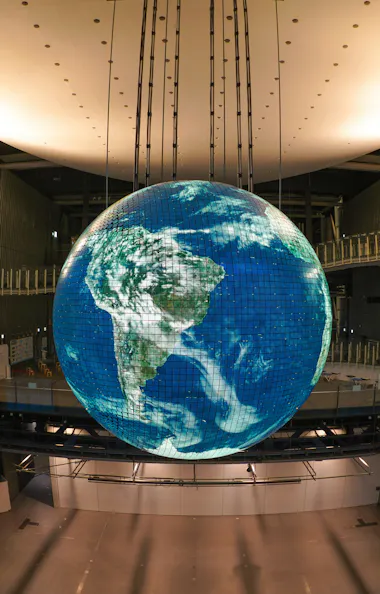 Miraikan Museum A large, illuminated globe hangs in the center of a spacious modern building, displaying a digital image of Earth with continents and oceans visible, viewed from above with South America in focus.