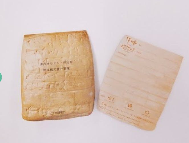 Two rectangular objects resembling slices of toast, one with Japanese text and the other designed like a postcard with labeled sections for address and message. Both have a toasted, slightly browned appearance.