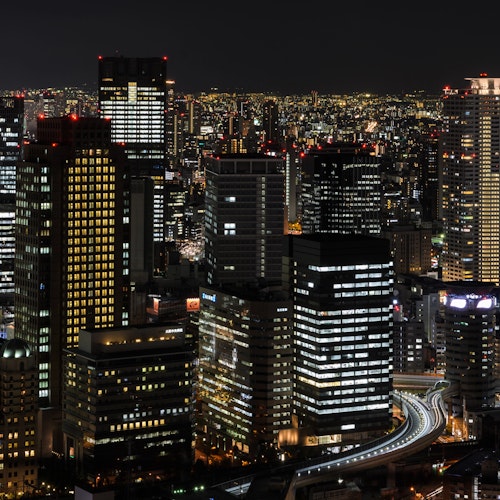 Umeda Sky Building in Osaka A nighttime cityscape featuring numerous illuminated high-rise buildings, creating a stunning array of lights. Roads and highways weave through the buildings, and the skyline is bathed in the soft glow of city lights under a dark sky.