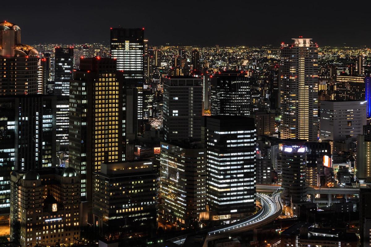 Umeda Sky Building in Osaka A nighttime cityscape featuring numerous illuminated high-rise buildings, creating a stunning array of lights. Roads and highways weave through the buildings, and the skyline is bathed in the soft glow of city lights under a dark sky.