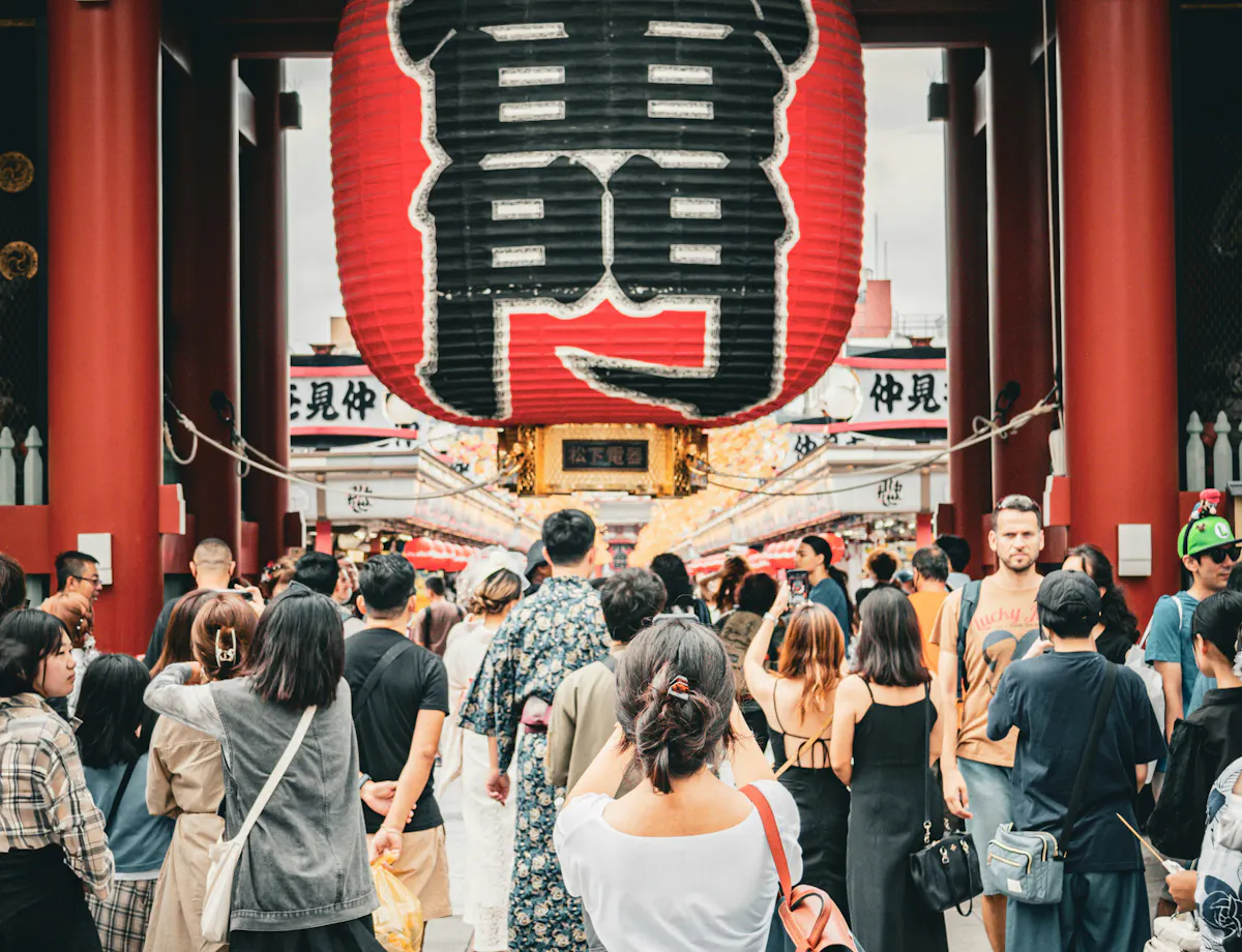 Kaminarimon Gate A crowd of people gathers in front of the large red lantern at the entrance of Senso-ji Temple in Tokyo, Japan, with traditional Japanese architecture and signs visible above.