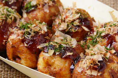 Close-up of takoyaki, Japanese octopus balls, topped with sauce, mayonnaise, dried seaweed, and bonito flakes, served in a wooden tray.