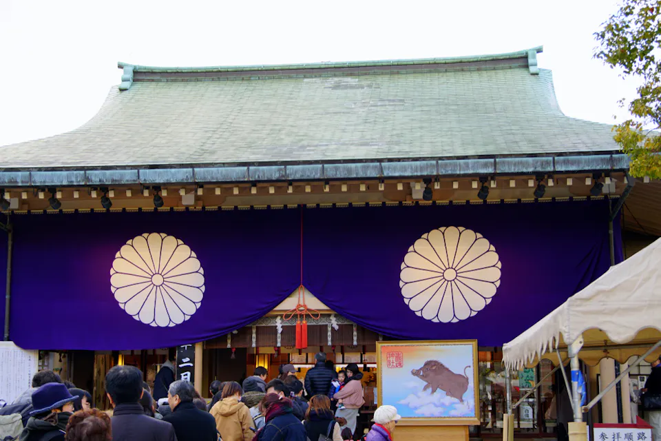 Ikukunitama Shrine , (Ikutama-san) is a Shinto shrine located in Tennoji-ku, Osaka Prefecture A crowd of people stands in front of a traditional Japanese shrine with a purple curtain adorned with two large, white chrysanthemum emblems. An artwork depicting a black ox on a cloud is displayed prominently near the entrance.