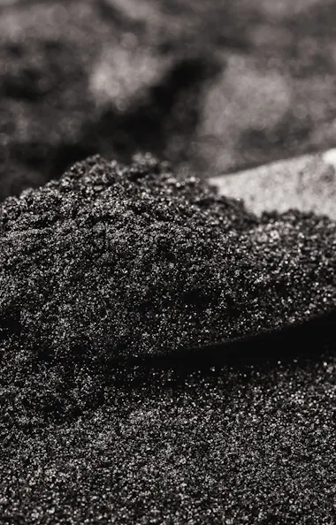 Sand A metal scoop is resting in a mound of fine, black granular powder, with shining particles reflecting light on the surface.