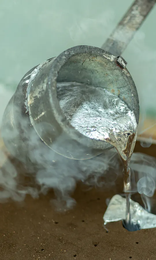 Sand Mold Casting A metal ladle pours hot, molten metal into a sand mold, with steam rising from the process. The scene depicts metal casting in a workshop environment.