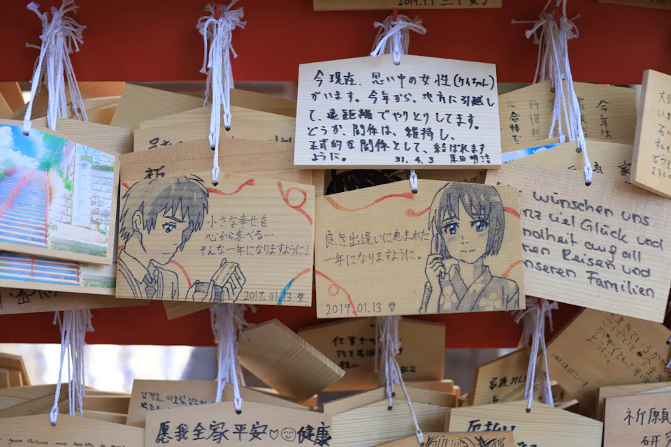 Fans leave ema with drawings of the Your Name characters at Suga Shrine. Wooden ema prayer plaques hanging at Suga Shrine, decorated with hand-drawn anime characters and handwritten wishes