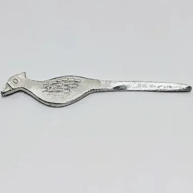 Sculpting Workshop A metallic object shaped like a bird with engraved feather details, featuring a pointed tail and a head with a beak, lying on a plain white background.