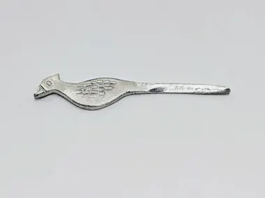 A metallic object shaped like a bird with engraved feather details, featuring a pointed tail and a head with a beak, lying on a plain white background.