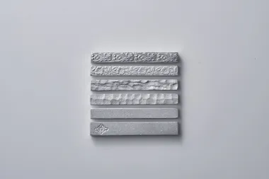 Seven silver metallic bars with different embossed patterns and textures are arranged horizontally in a neat vertical stack on a plain white background.