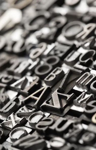 Engraving A close-up view of assorted metal letterpress type blocks arranged tightly together, featuring various letters, numbers, and symbols in different fonts and sizes, with a shallow depth of field.