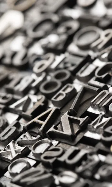 Engraving A close-up view of assorted metal letterpress type blocks arranged tightly together, featuring various letters, numbers, and symbols in different fonts and sizes, with a shallow depth of field.