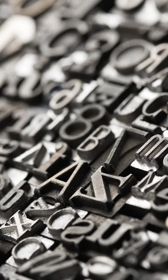 Engraving A close-up view of assorted metal letterpress type blocks arranged tightly together, featuring various letters, numbers, and symbols in different fonts and sizes, with a shallow depth of field.