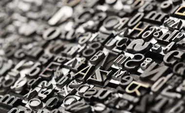 A close-up view of assorted metal letterpress type blocks arranged tightly together, featuring various letters, numbers, and symbols in different fonts and sizes, with a shallow depth of field.