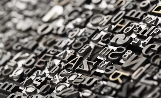 A close-up view of assorted metal letterpress type blocks arranged tightly together, featuring various letters, numbers, and symbols in different fonts and sizes, with a shallow depth of field.