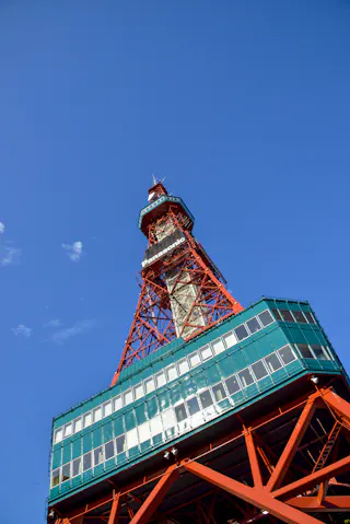 A low-angle view of the red and white Sapporo TV Tower against a clear blue sky, with the tower’s observation deck and structural details visible.