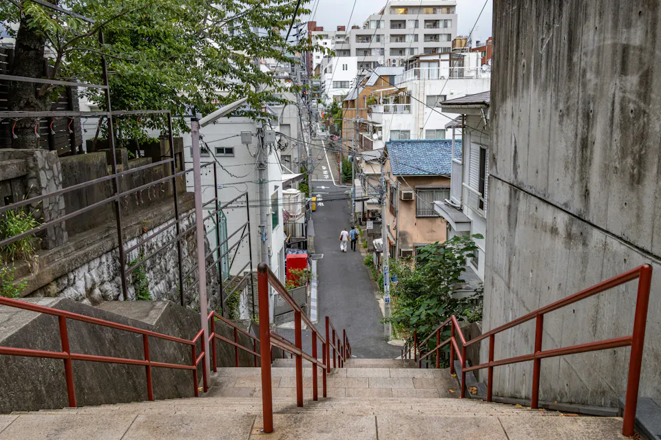 The stairs below Suga Shrine appear in the final scene of Your Name. Stone stairs with red handrails running down a narrow residential street in Yotsuya, Tokyo