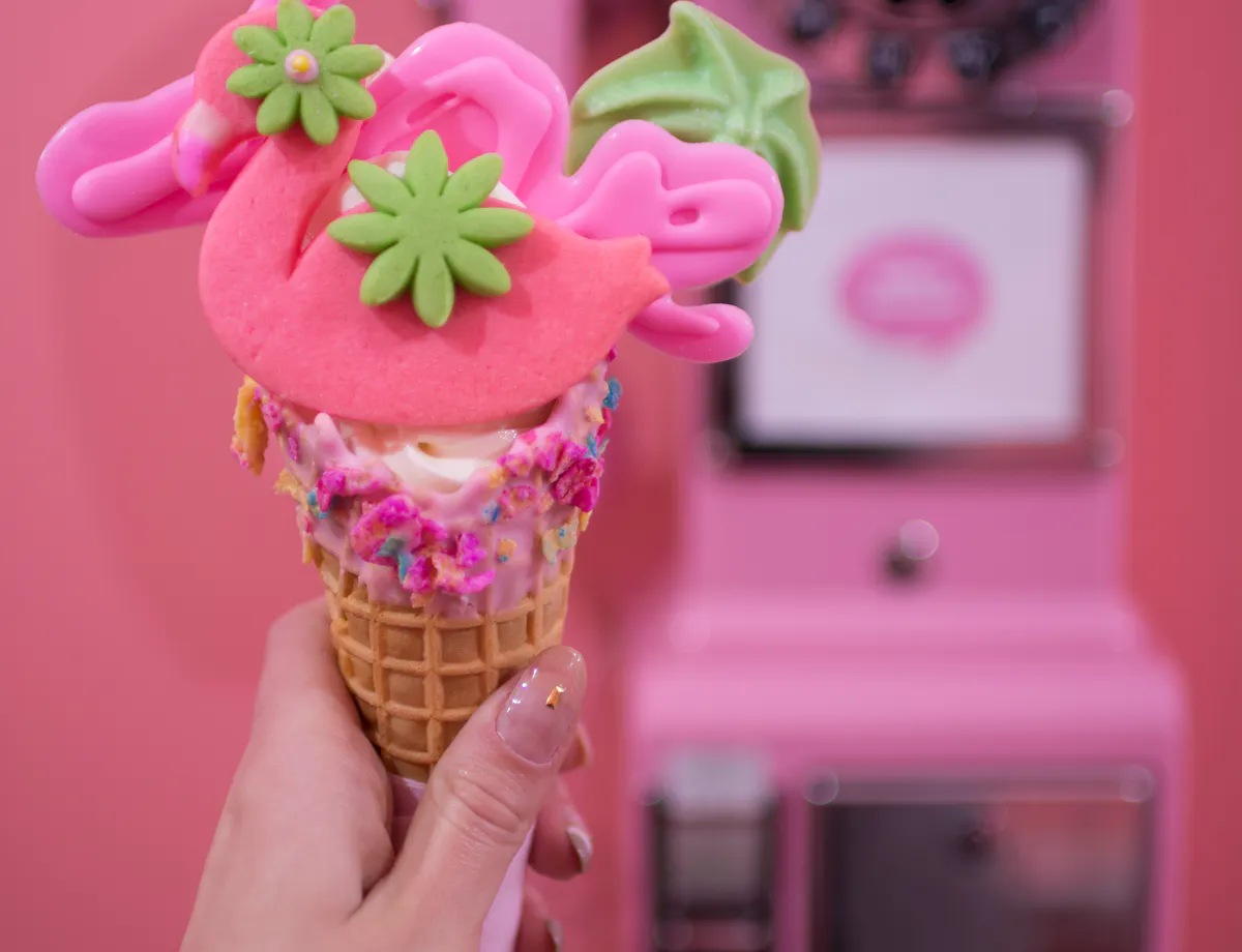 Harajuku Food Tour A hand holds a colorful ice cream cone topped with pink and green decorative cookies in front of a vintage pink rotary payphone on a matching pink background.