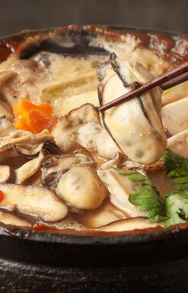 Oyster and Vegetable Miso Hot Pot A steaming hot pot filled with oysters, mushrooms, vegetables, and broth, with chopsticks lifting an oyster from the pot.