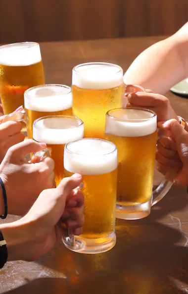 Toast Several people raise glasses of beer together over a wooden table, toasting in a celebratory gesture. The scene is bright and cheerful, suggesting a social gathering or celebration.