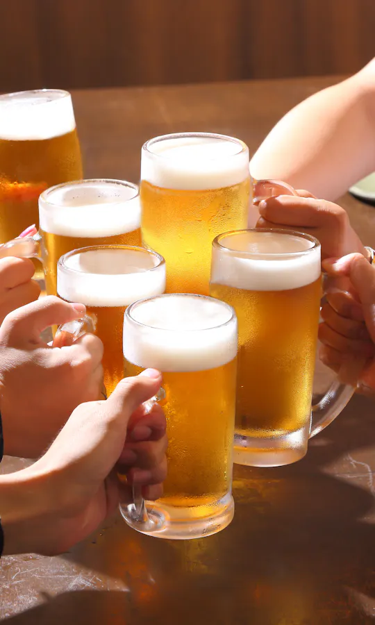 Toast Several people raise glasses of beer together over a wooden table, toasting in a celebratory gesture. The scene is bright and cheerful, suggesting a social gathering or celebration.