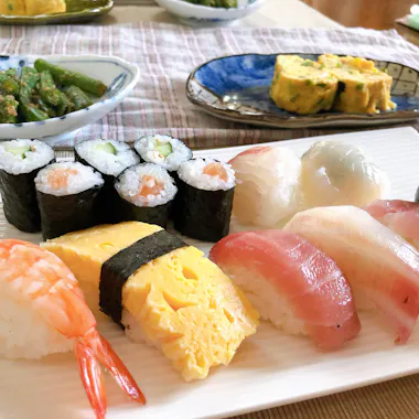 Sushi Class Tokyo A plate of assorted sushi including nigiri with shrimp, egg, and fish, as well as maki rolls with cucumber and salmon. In the background are side dishes of asparagus and tamagoyaki (Japanese omelette).