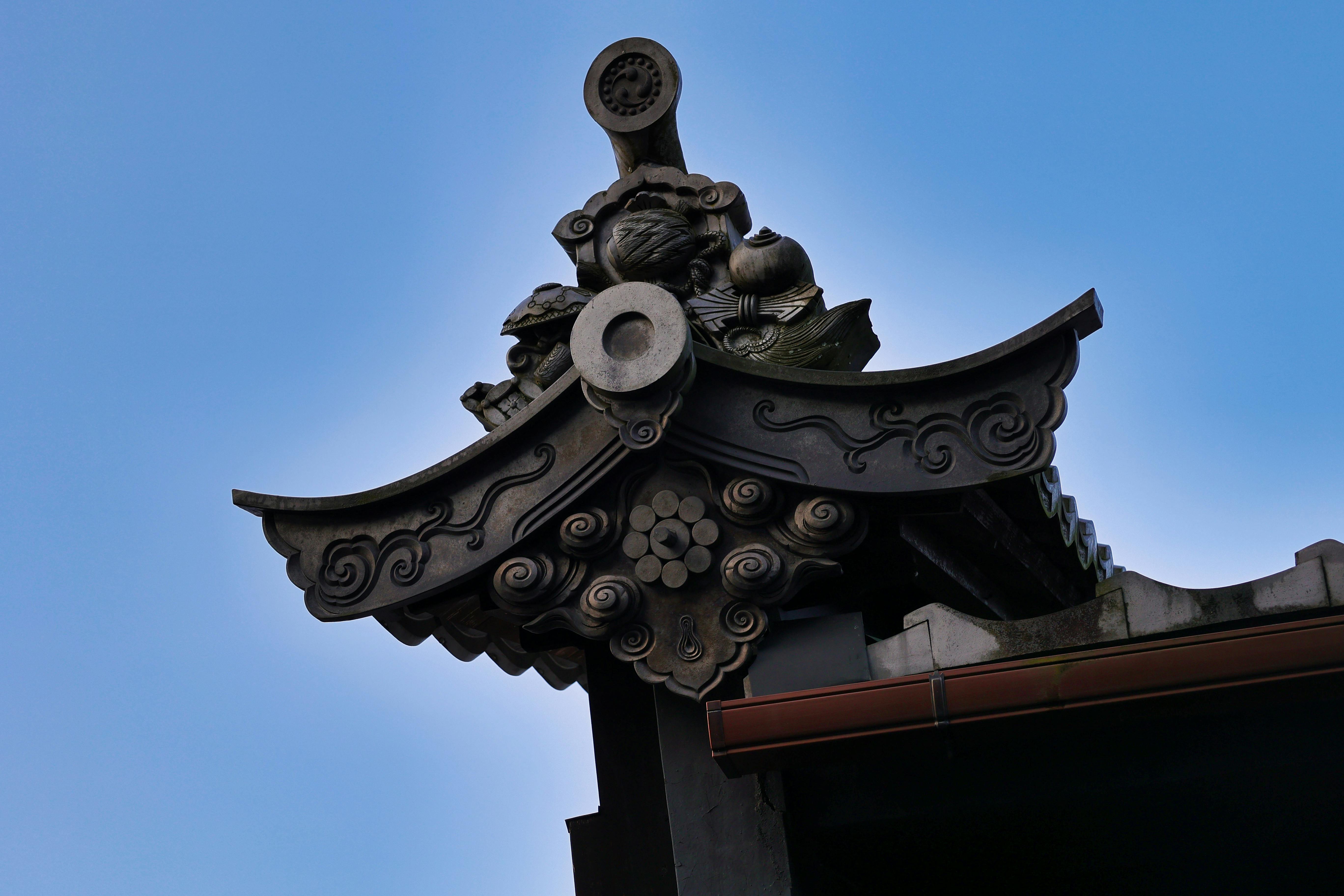 Ornate traditional Japanese roof detail with intricate carvings and decorative elements against a clear blue sky.