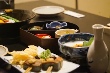 A table set with various Japanese dishes, including skewered food, bowls of soup, dipping sauces, a sake bottle, and a plate with tempura, arranged neatly for a meal.