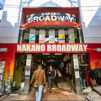 Nakano Broadway Entrance of Nakano Broadway shopping mall in Tokyo, Japan, with a red and white sign above and people entering and exiting. Vending machines and colorful advertisements line both sides of the entrance.