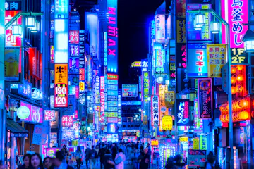 A vibrant city street at night filled with colorful neon signs in Japanese, crowded with people walking under the glowing lights. The scene is lively and bustling, creating a futuristic and energetic urban atmosphere.