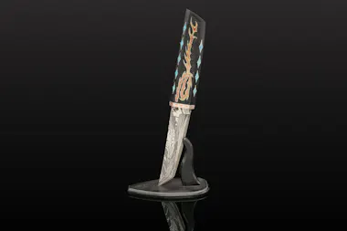 A decorative knife with an intricately patterned blade and a handle featuring colorful, artistic inlays, displayed upright in a black, curved stand against a dark background.