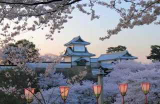 A traditional Japanese castle surrounded by blooming cherry blossom trees, with colorful lanterns in the foreground and a soft pastel sky in the background.