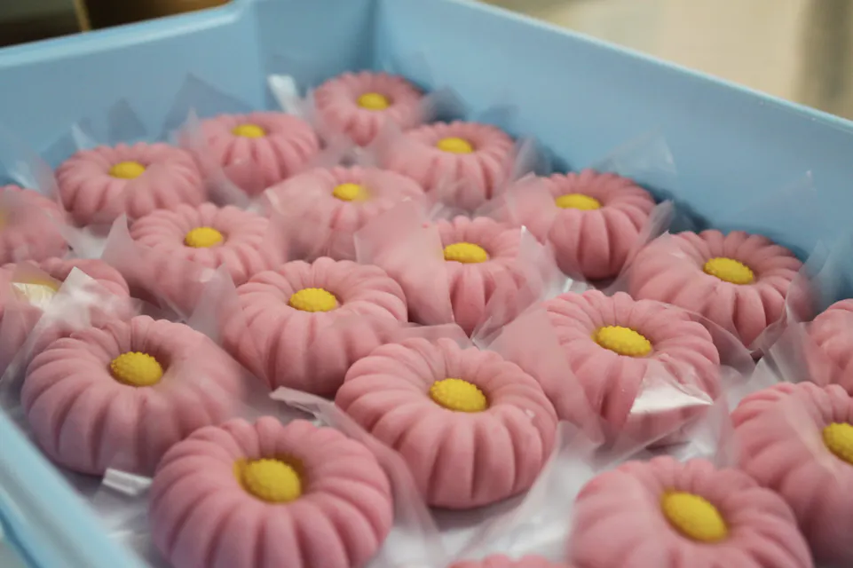 A blue tray filled with individually wrapped pink flower-shaped sweets, each with a yellow center, resembling daisies.
