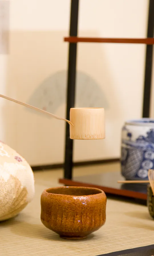 Tea Ceremony A person in a traditional kimono prepares tea, holding a bamboo ladle over a ceramic bowl, with tea ceremony utensils arranged neatly on a tatami mat.