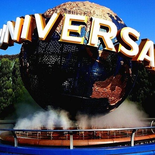 Universal Studios Japan The image shows a large globe with the word "UNIVERSAL" in bold letters wrapped around it. The globe is surrounded by mist and set against a backdrop of trees and a bright blue sky.
