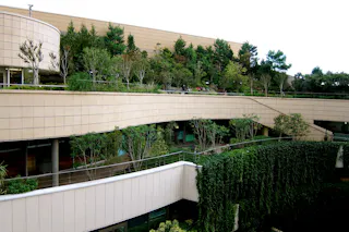 A modern multi-level building features large curved terraces with lush greenery and trees, creating a rooftop garden and vertical green walls, blending architecture with nature under a bright sky.