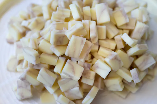 A close-up view of a pile of small, square white chocolate pieces with brown marbled swirls on a white surface.