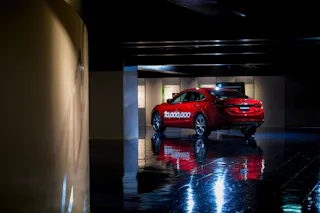 A red car with "10,000,000" written on the side is parked indoors under dim lighting, its reflection visible on the shiny black floor.